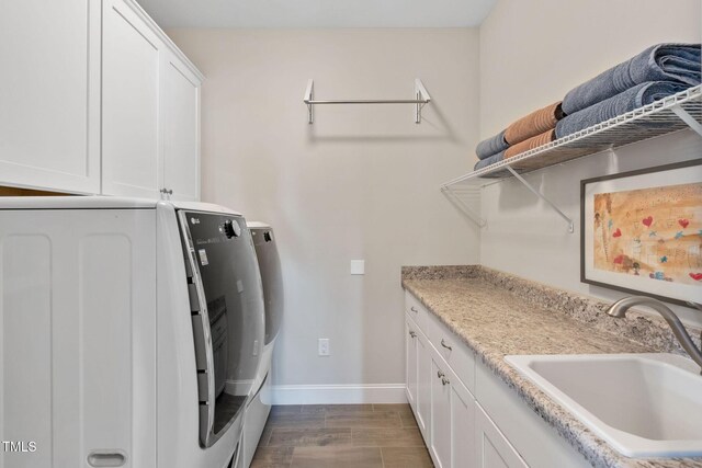 clothes washing area featuring washing machine and clothes dryer, baseboards, cabinet space, and dark wood finished floors