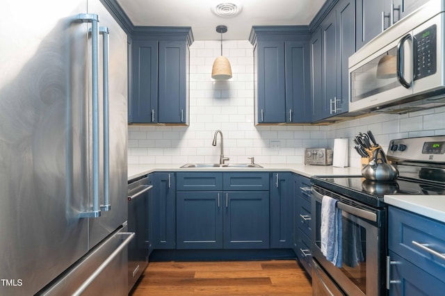 kitchen featuring appliances with stainless steel finishes, a sink, blue cabinetry, and tasteful backsplash
