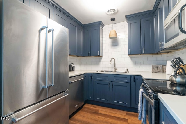 kitchen with appliances with stainless steel finishes, a sink, blue cabinetry, backsplash, and light countertops