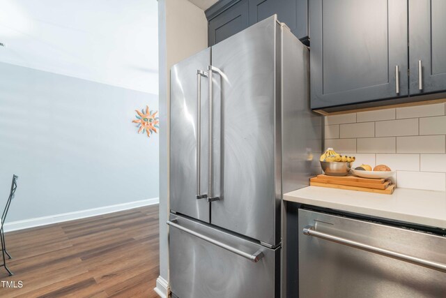 kitchen with appliances with stainless steel finishes, dark wood-style floors, backsplash, light countertops, and baseboards