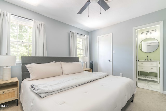 bedroom with ensuite bath, a ceiling fan, a sink, and light carpet