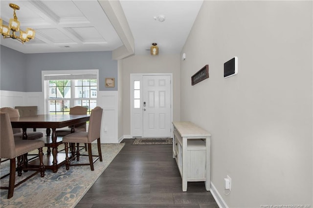 entrance foyer with a notable chandelier, coffered ceiling, dark wood-style flooring, a wainscoted wall, and beamed ceiling