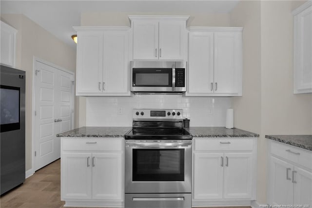 kitchen featuring stainless steel appliances, tasteful backsplash, dark stone countertops, and white cabinets