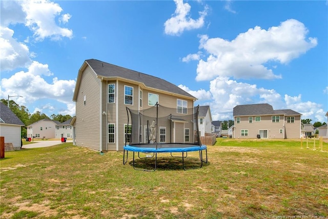 back of property with a trampoline, a yard, and a residential view