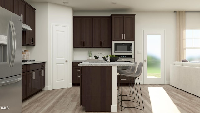 kitchen featuring light wood-style flooring, dark brown cabinets, a sink, decorative backsplash, and stainless steel appliances