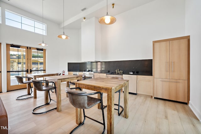 kitchen with a towering ceiling, dishwasher, decorative backsplash, and light wood-style floors