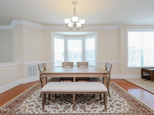 dining space with a chandelier, wood finished floors, healthy amount of natural light, and crown molding