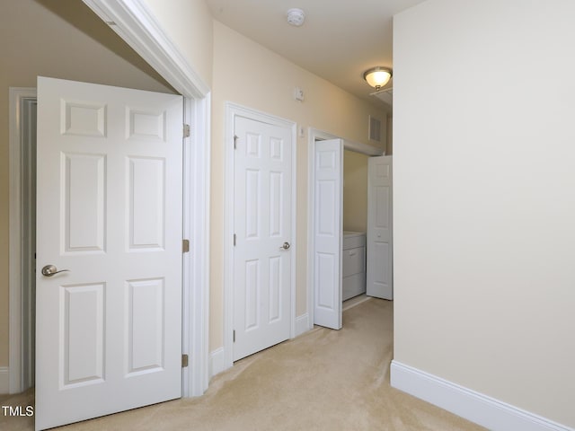 corridor featuring washer / clothes dryer, light carpet, and baseboards