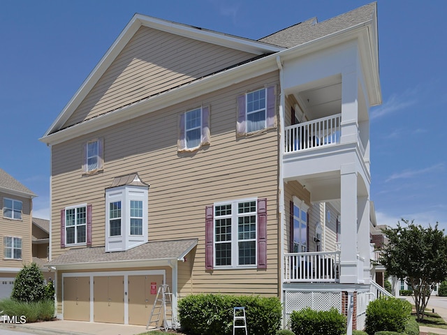 view of front of property with a balcony, an attached garage, driveway, and roof with shingles