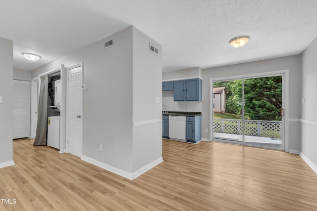 unfurnished living room with light wood-style flooring, baseboards, a textured ceiling, and stacked washer / drying machine