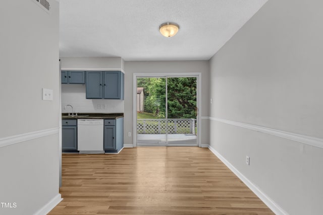kitchen featuring dishwasher, a sink, light wood-style floors, backsplash, and baseboards
