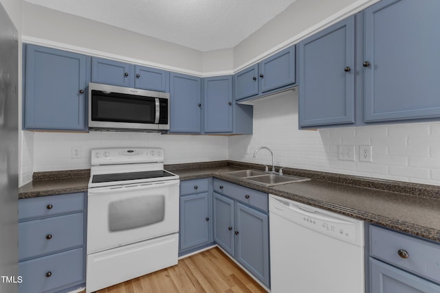 kitchen featuring white appliances, a sink, blue cabinetry, dark countertops, and a textured ceiling