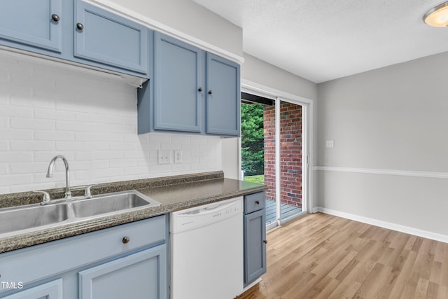 kitchen featuring white dishwasher, a sink, dark countertops, blue cabinets, and light wood finished floors