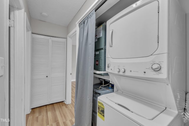laundry area featuring stacked washer and clothes dryer, light wood-type flooring, and a textured ceiling