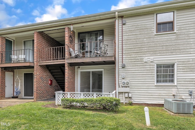 rear view of property with central AC, a lawn, a balcony, and brick siding
