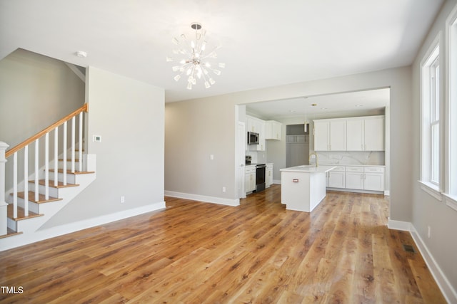 509 Olive Branch Rd, Durham, NC 27703 - unfurnished living room featuring stairway, a chandelier, light wood-style flooring, and baseboards