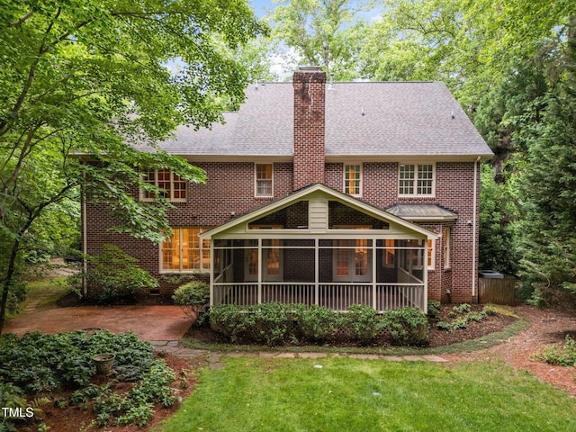 rear view of property with a sunroom, a shingled roof, a chimney, a lawn, and brick siding