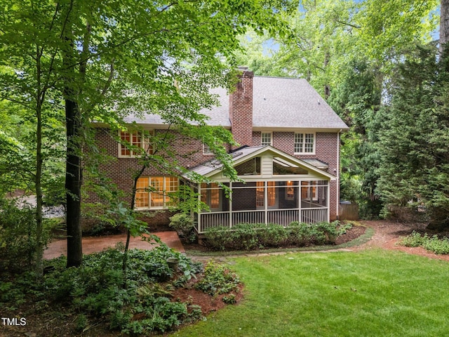 rear view of property featuring a yard, a chimney, a sunroom, and brick siding