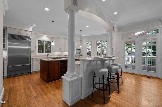kitchen with appliances with stainless steel finishes, a kitchen island, decorative columns, ornamental molding, and light wood-style flooring