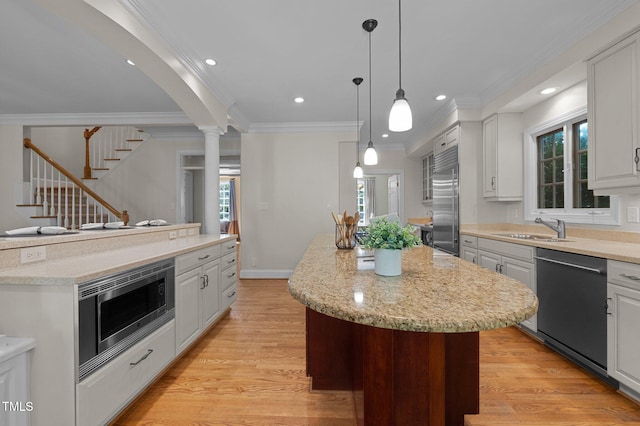 kitchen featuring a center island, built in appliances, a sink, ornamental molding, and light wood-style floors