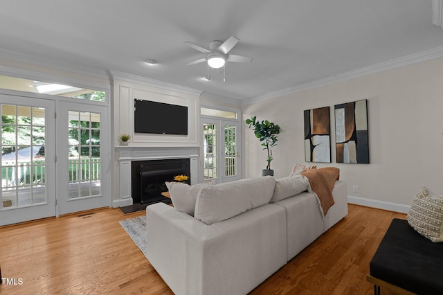 living room with ornamental molding, healthy amount of natural light, ceiling fan, a fireplace with raised hearth, and light wood finished floors