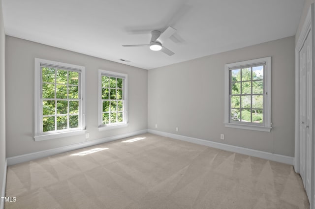 empty room featuring baseboards, healthy amount of natural light, light colored carpet, and a ceiling fan