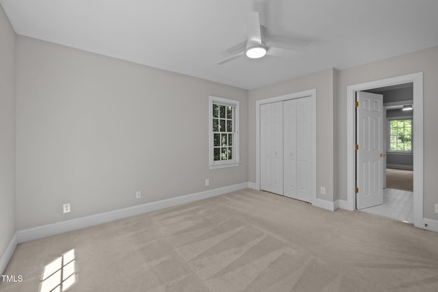 unfurnished bedroom featuring light colored carpet, baseboards, a closet, and ceiling fan
