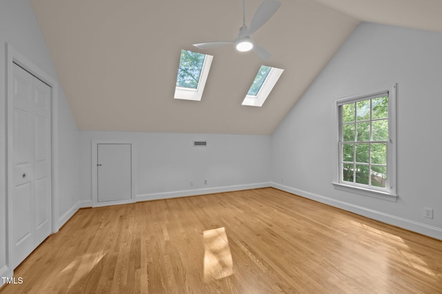 additional living space with light wood-style flooring, vaulted ceiling, a skylight, a ceiling fan, and baseboards