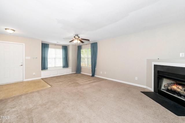 unfurnished living room with carpet flooring, a ceiling fan, a fireplace with flush hearth, and baseboards