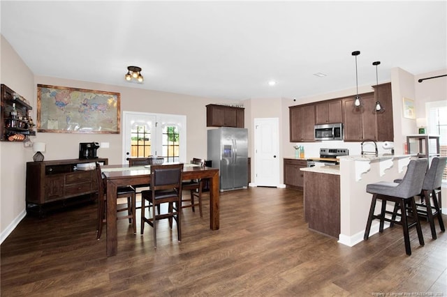 kitchen featuring a peninsula, stainless steel appliances, a kitchen breakfast bar, dark brown cabinetry, and dark wood-style flooring