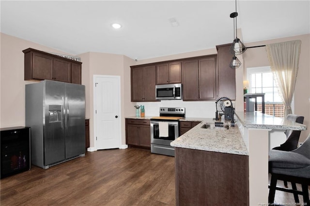 kitchen with a sink, a peninsula, stainless steel appliances, dark wood-style floors, and dark brown cabinets