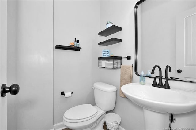 bathroom featuring baseboards, toilet, and a sink