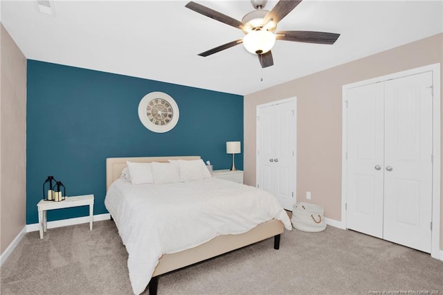 carpeted bedroom with two closets, baseboards, a ceiling fan, and an accent wall