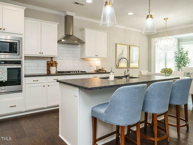 kitchen featuring stainless steel appliances, wall chimney range hood, a sink, dark wood-style flooring, and crown molding