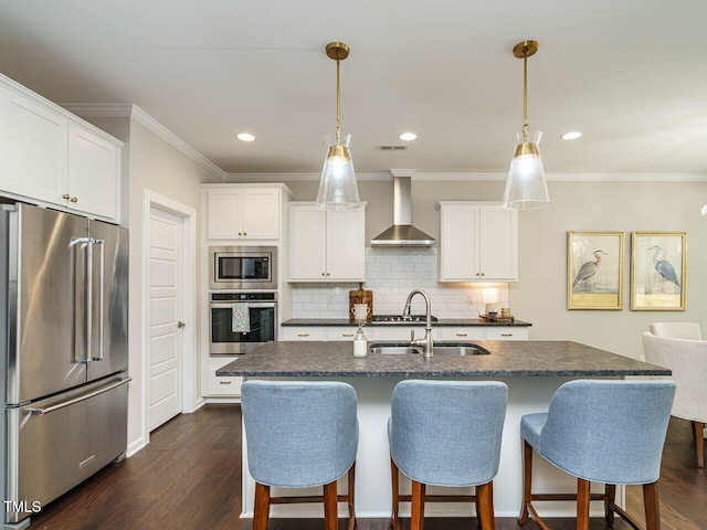 kitchen with stainless steel appliances, wall chimney range hood, a sink, a breakfast bar, and crown molding