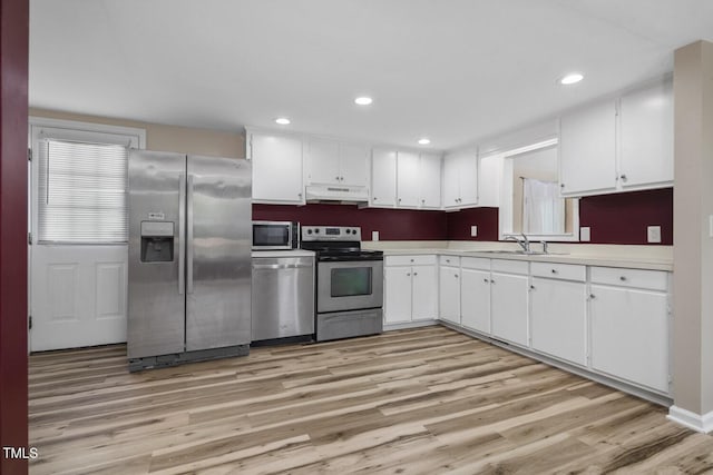 kitchen with stainless steel appliances, under cabinet range hood, a sink, light wood-style floors, and white cabinets
