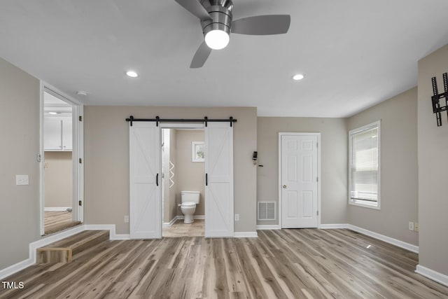 unfurnished bedroom featuring light wood-type flooring, a barn door, baseboards, recessed lighting, and ensuite bath