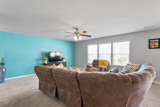 living area with light colored carpet, ceiling fan, baseboards, and a textured ceiling