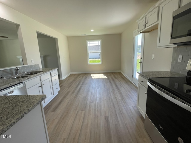 kitchen featuring baseboards, a sink, decorative backsplash, stainless steel appliances, and light wood-type flooring