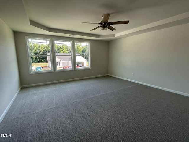 unfurnished room with a tray ceiling, dark colored carpet, baseboards, and ceiling fan