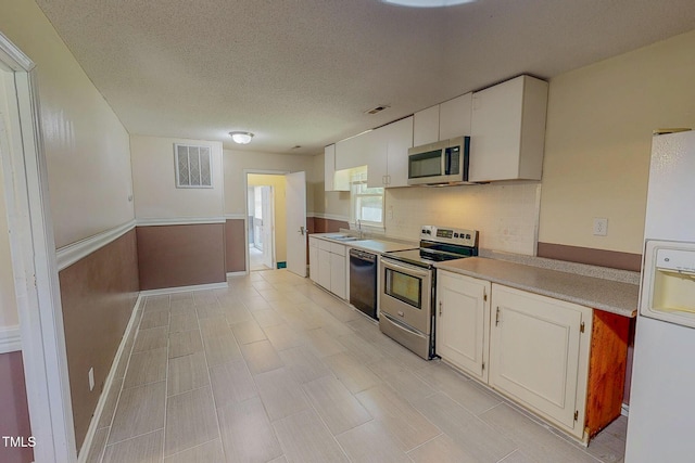 kitchen with stainless steel appliances, tasteful backsplash, white cabinets, light countertops, and a textured ceiling