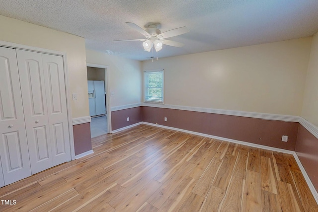 unfurnished bedroom featuring white fridge with ice dispenser, light wood finished floors, a closet, baseboards, and a textured ceiling