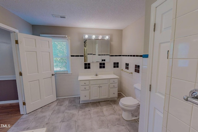 bathroom featuring tile walls, vanity, toilet, a textured ceiling, and tile patterned floors