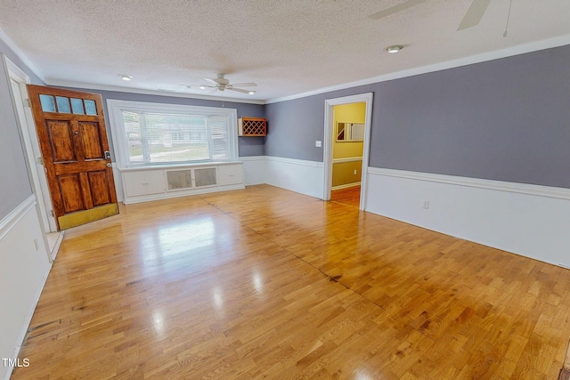 empty room with ceiling fan, a textured ceiling, a wainscoted wall, wood finished floors, and ornamental molding