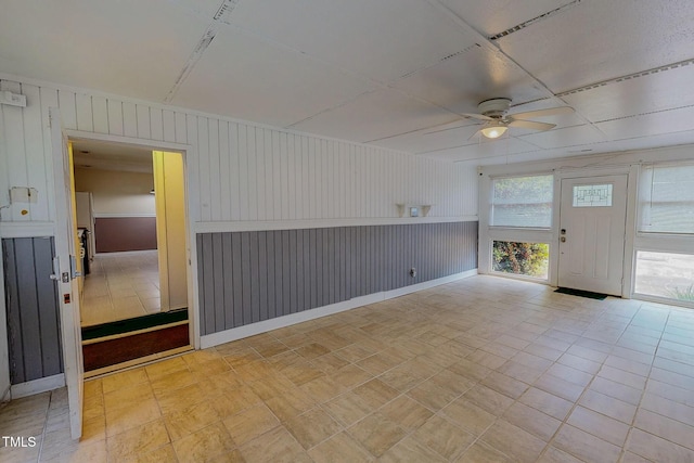 unfurnished room with a ceiling fan, wooden walls, and baseboards