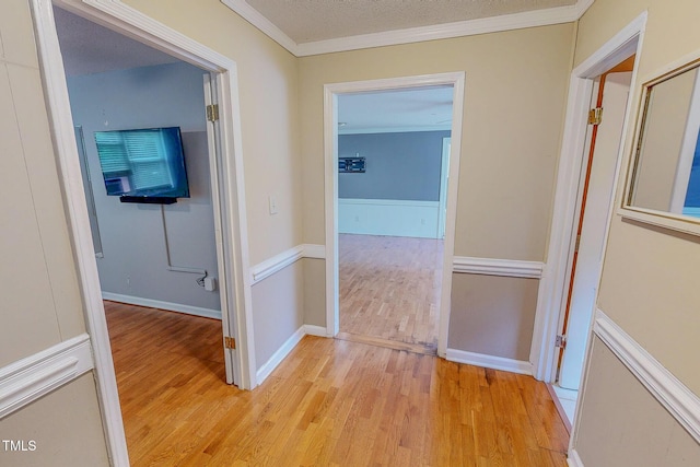 hallway with light wood-style flooring, crown molding, and a textured ceiling