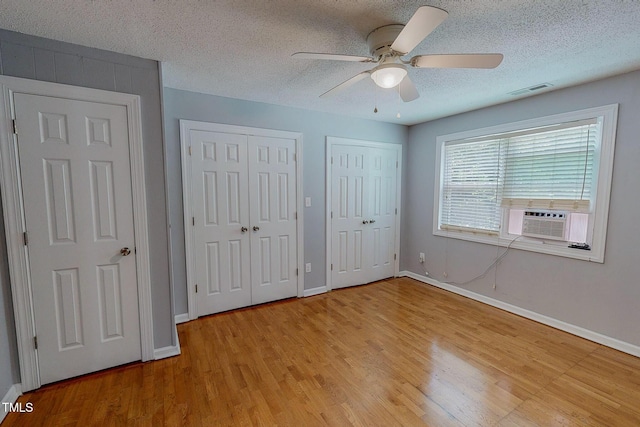 unfurnished bedroom featuring cooling unit, multiple closets, light wood-type flooring, baseboards, and a textured ceiling
