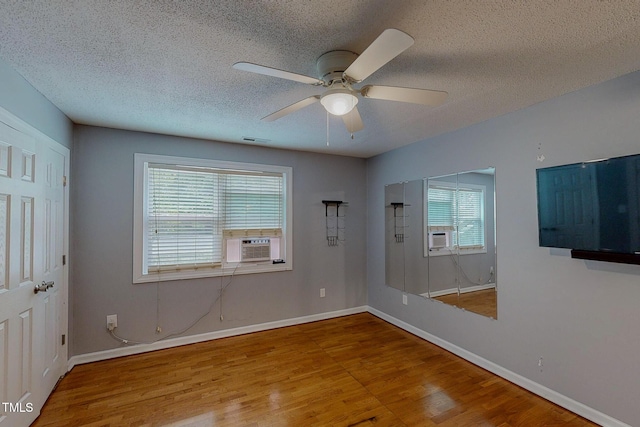 unfurnished room featuring wood finished floors, ceiling fan, a textured ceiling, baseboards, and cooling unit