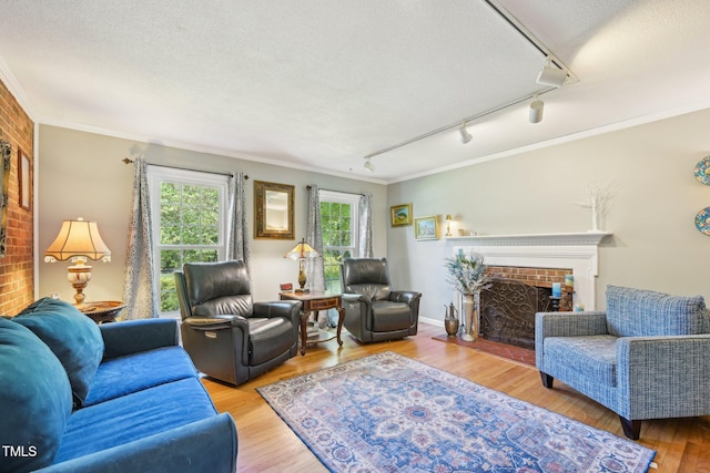 living area featuring track lighting, a textured ceiling, crown molding, a brick fireplace, and wood finished floors