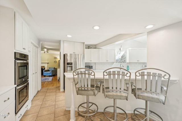 kitchen with appliances with stainless steel finishes, a kitchen breakfast bar, light countertops, white cabinetry, and recessed lighting